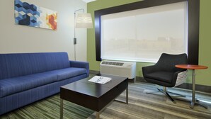 Una habitación de hotel moderna con un sofá azul, una mesita, un sillón negro, una mesa redonda y un amplio ventanal con vistas a la ciudad.