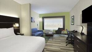 Habitación de hotel con una cama grande, un escritorio con computadora, una silla, un sofá y un ventanal con vistas.