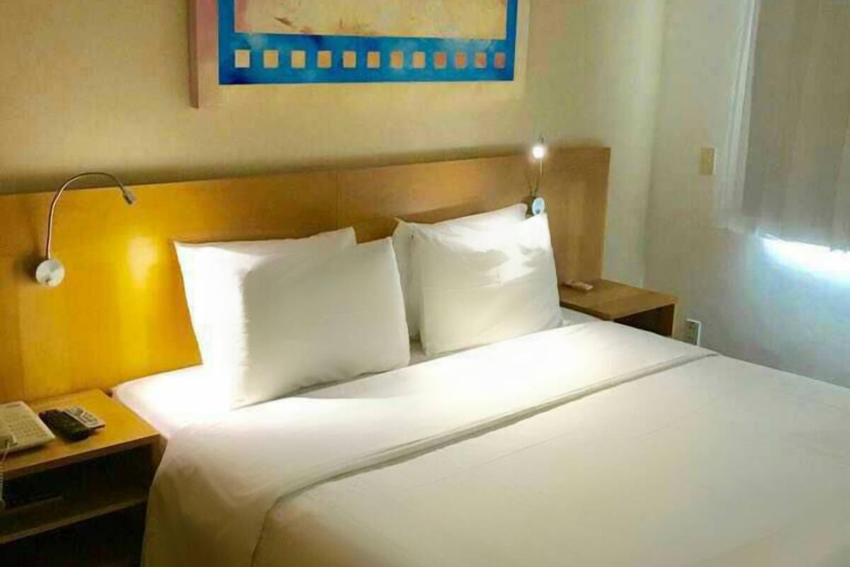 A hotel room with a large bed, a nightstand with a phone, a lamp, and a painting on the wall.