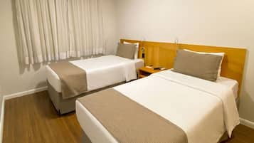 Ein Hotelzimmer mit zwei Betten, einem Holz-Kopfteil, einem Nachttisch, einer Lampe und einem fenster mit Vorhängen.
