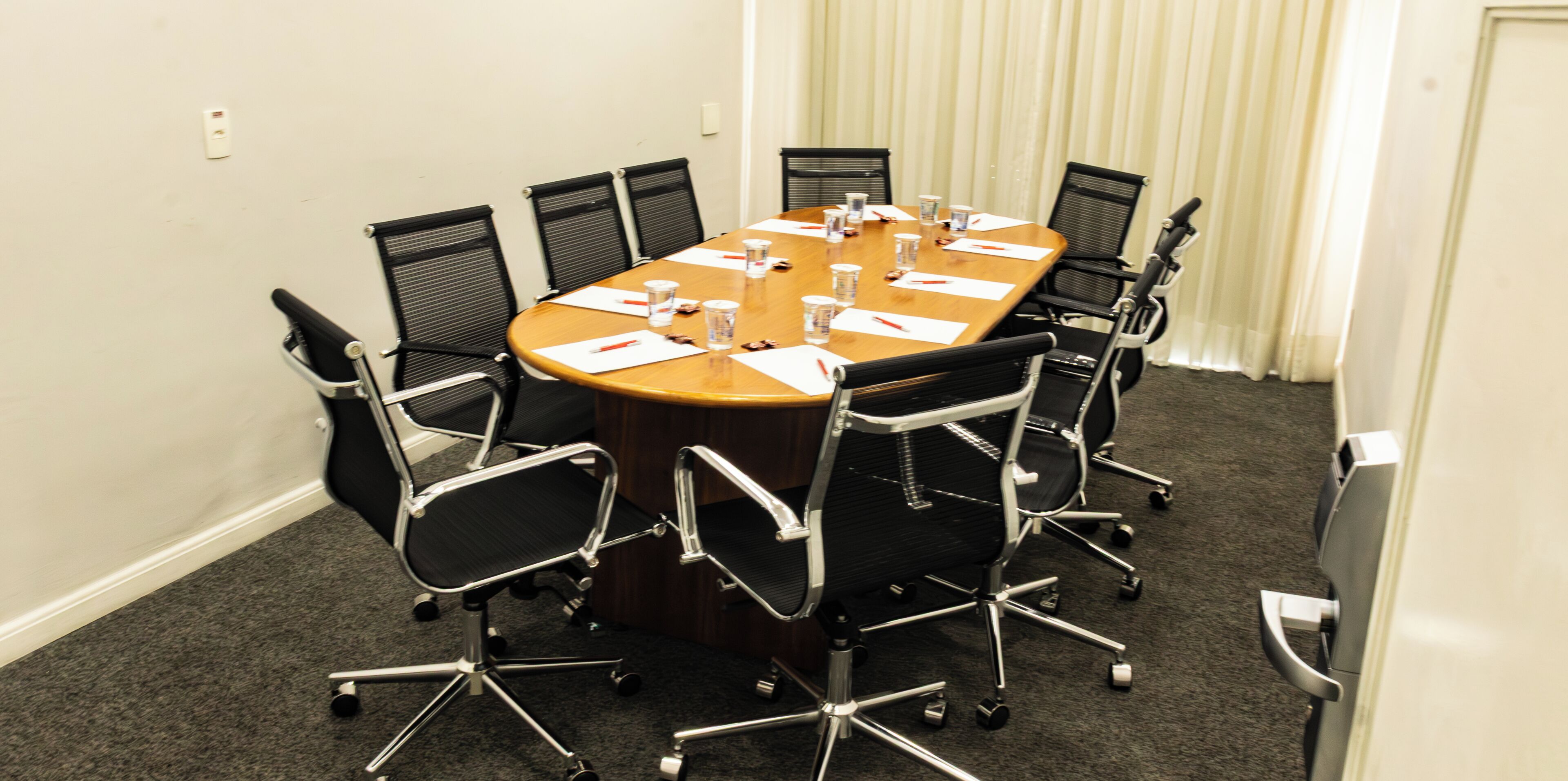 Una sala de conferencias con una mesa rectangular, sillas de oficina negras y piso alfombrado.