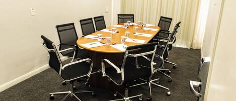 Ein Konferenzraum mit einem rechteckigen Tisch, schwarzen Bürostühlen und Teppichboden.