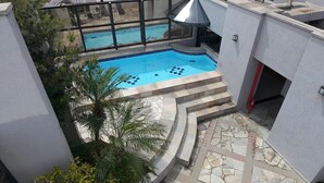 A rooftop swimming pool with a glass enclosure, surrounded by a stone-tiled deck and palm trees. - Marsala Apart Hotel (Mogi das Cruzes)