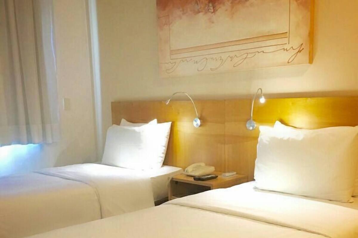 A hotel room with two beds, a nightstand with a phone, and a painting on the wall.