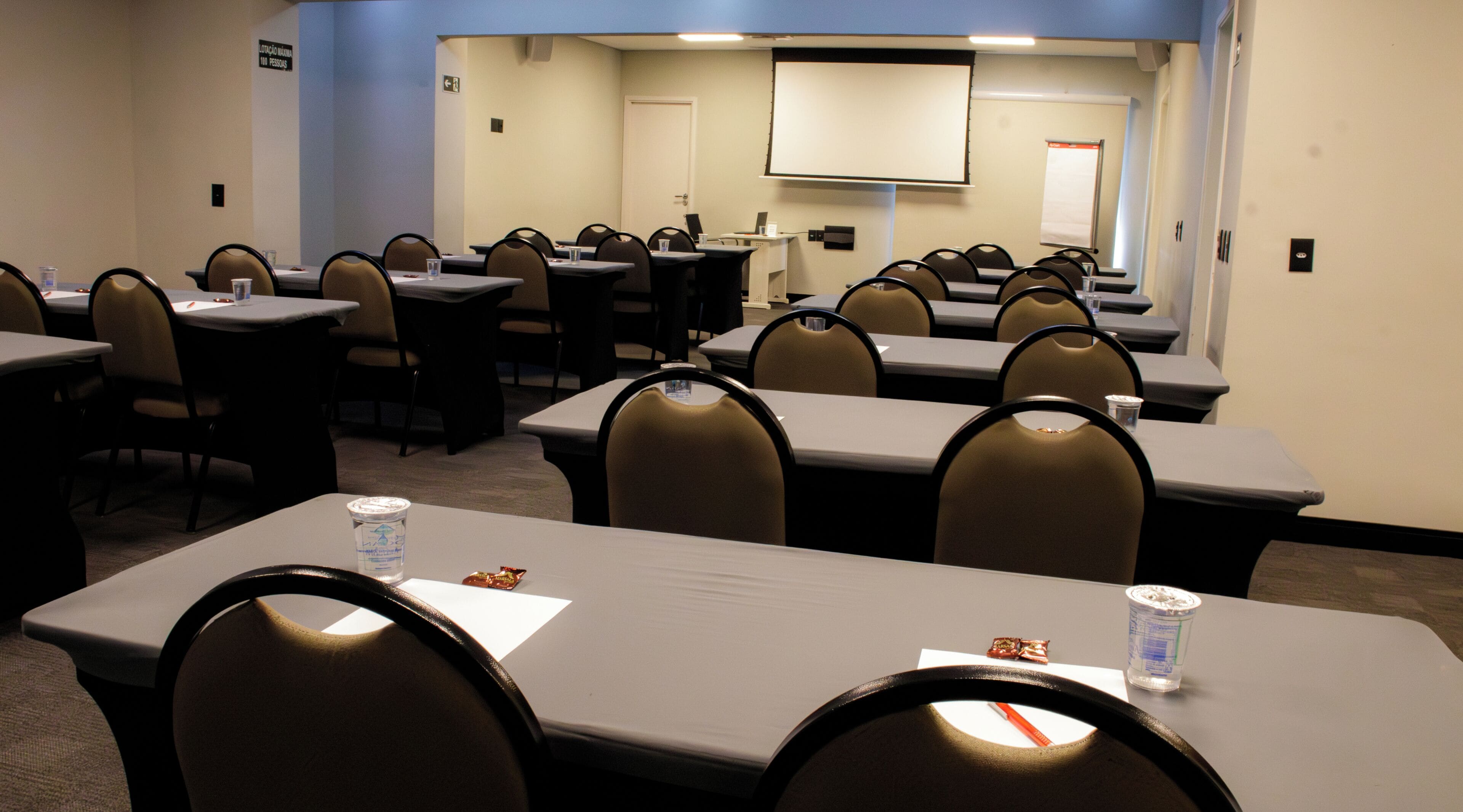 A conference room with tables, chairs, a projector screen, and a whiteboard.