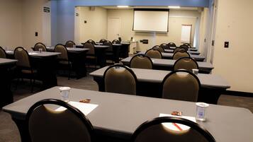 A conference room with tables, chairs, a projector screen, and a whiteboard.