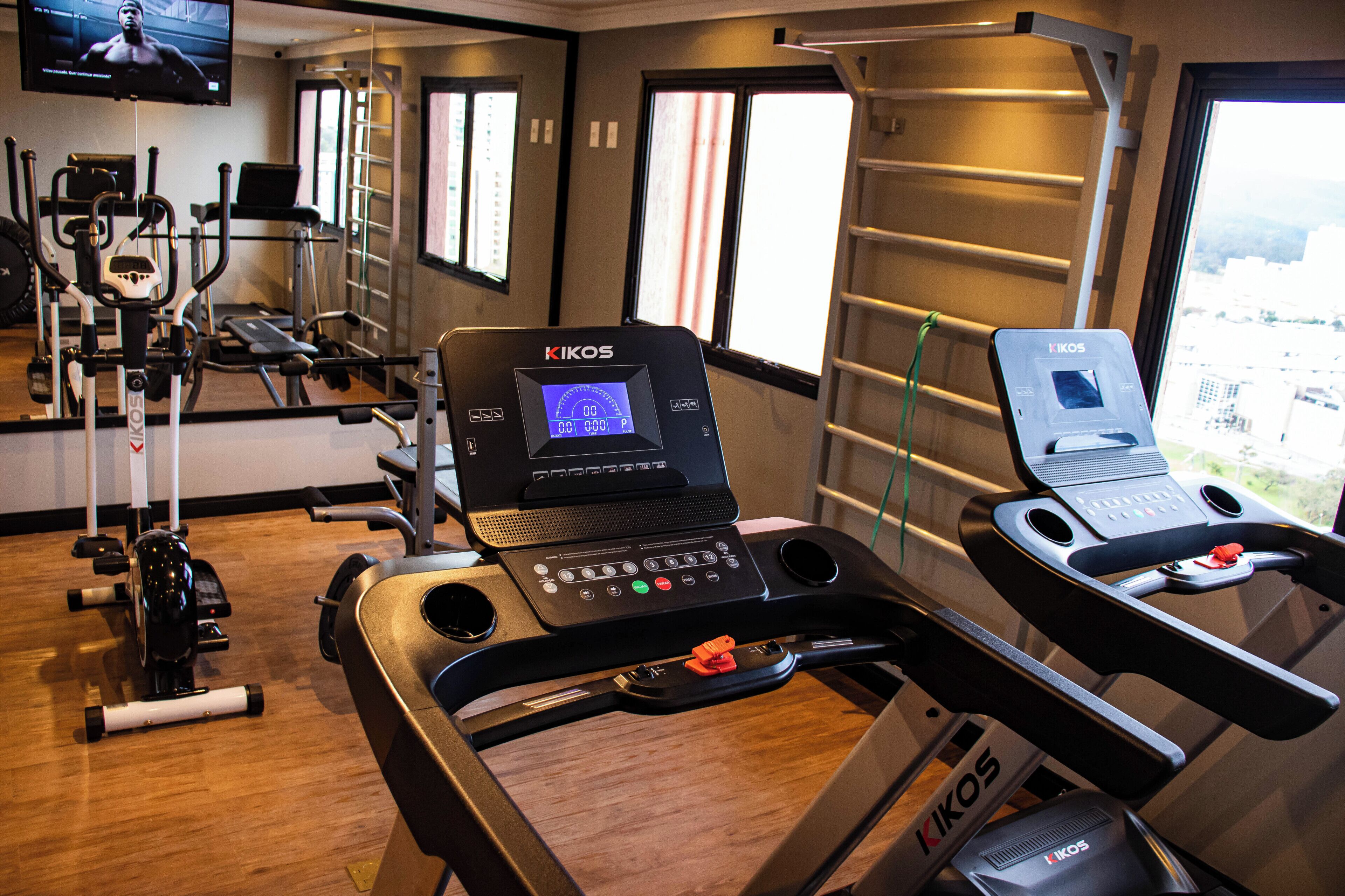 Un gimnasio con diversos equipos de ejercicio, incluyendo cintas de correr y bicicletas estáticas, y un ordenador portátil sobre una de las bicicletas.