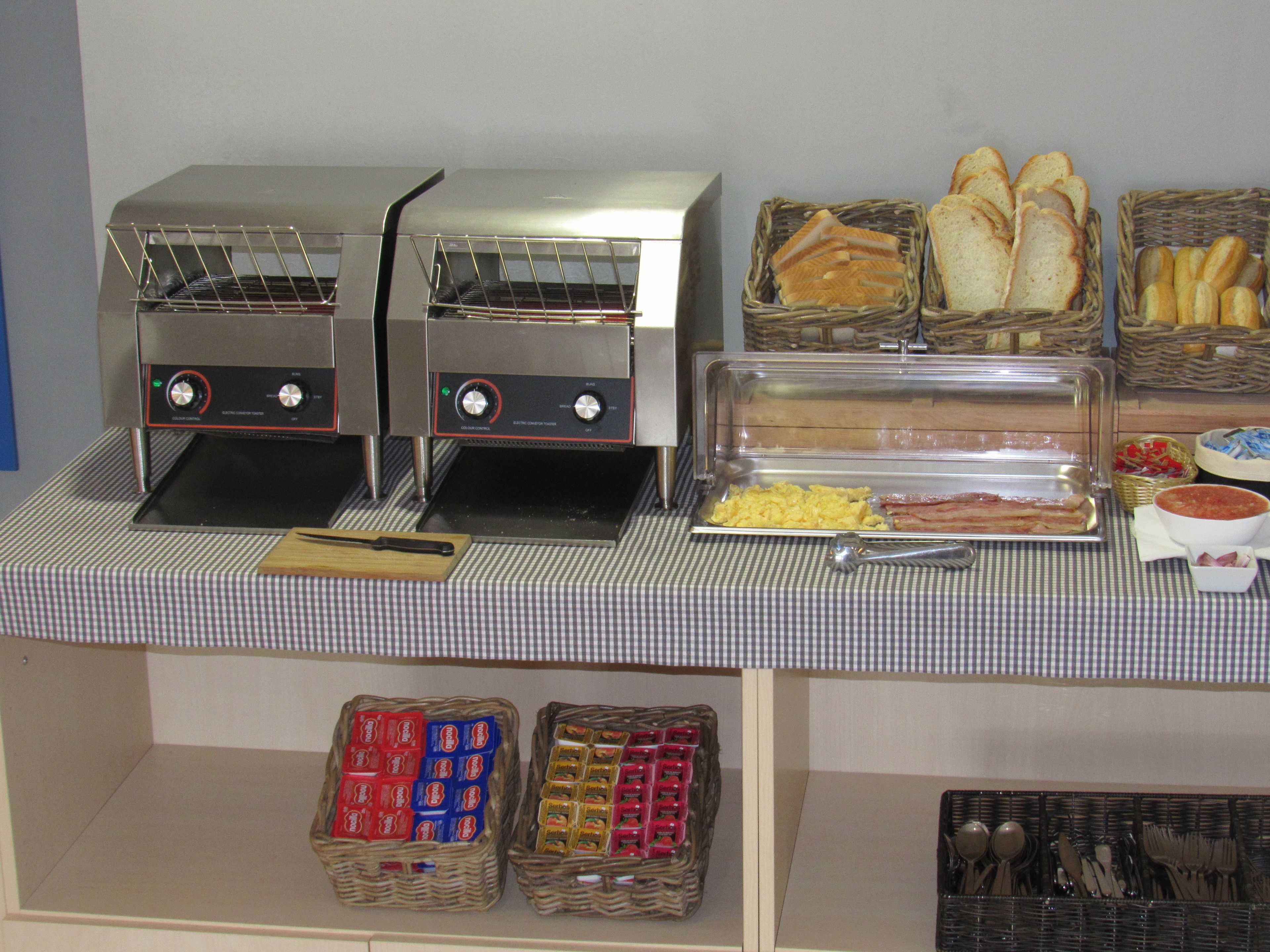 A buffet setup with two toasters, baskets of bread, and condiments.