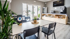 A modern hotel room with a dining area, a flat-screen TV, a coffee machine, and a potted plant. - Aparthotel Nelva Resort (Alayor)