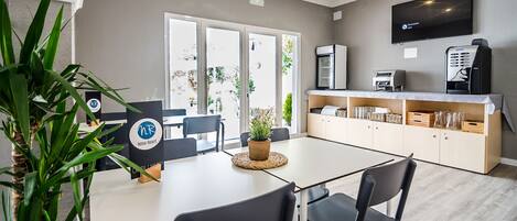 Una habitación de hotel moderna con zona de comedor, televisor de pantalla plana, cafetera y planta en maceta.