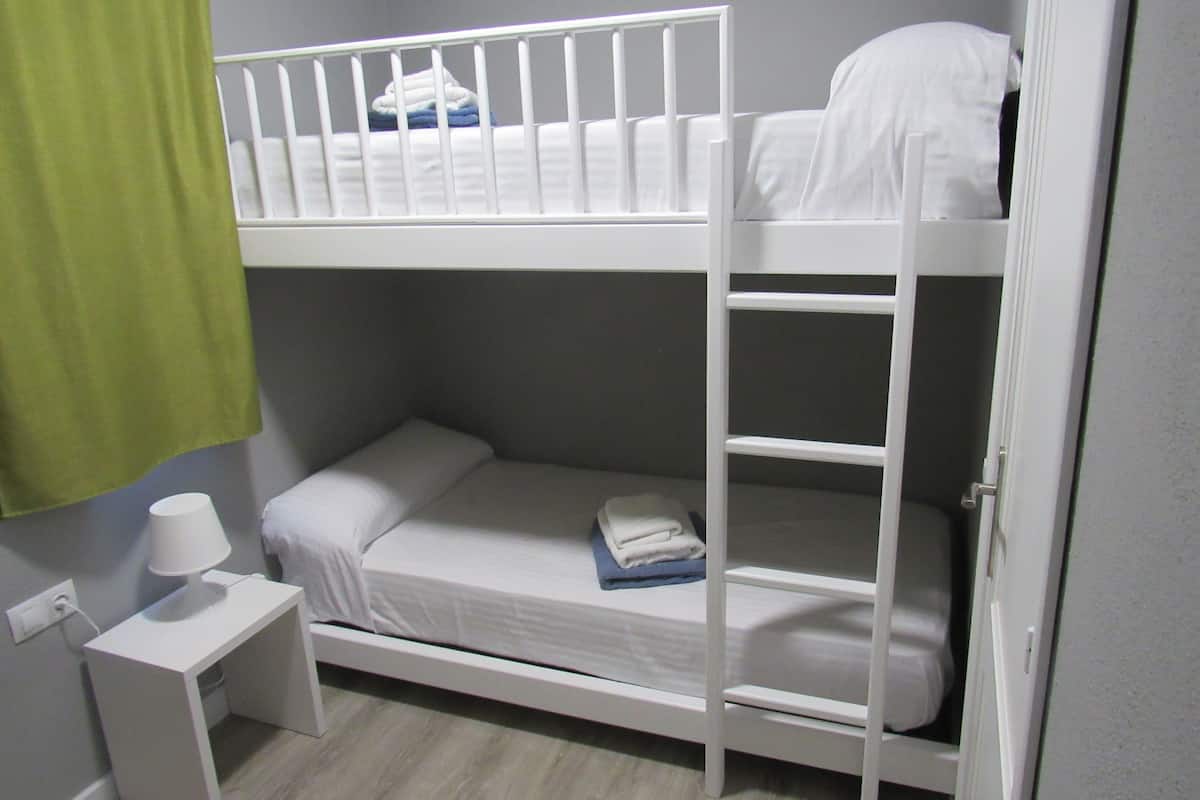 Ein Schlafzimmer mit Etagenbett, einem kleinen Nachttisch und einem grünen Vorhang.