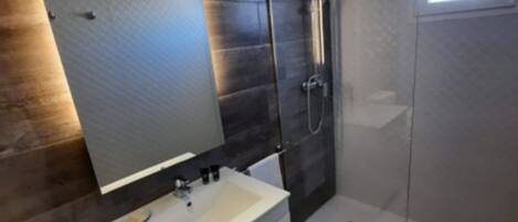 A modern bathroom with a large mirror, a white sink, and a glass-enclosed shower.