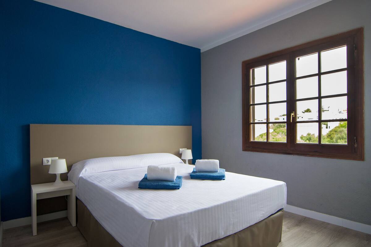 Ein Hotelzimmer mit Bett, zwei Nachttischen, einem Fenster mit Blick und einer blauen Akzentwand.