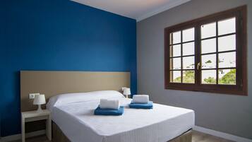A hotel room with a bed, two bedside tables, a window with a view, and a blue accent wall.