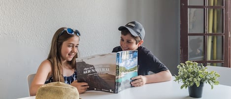 Two people sitting at a table with a book and a hat.