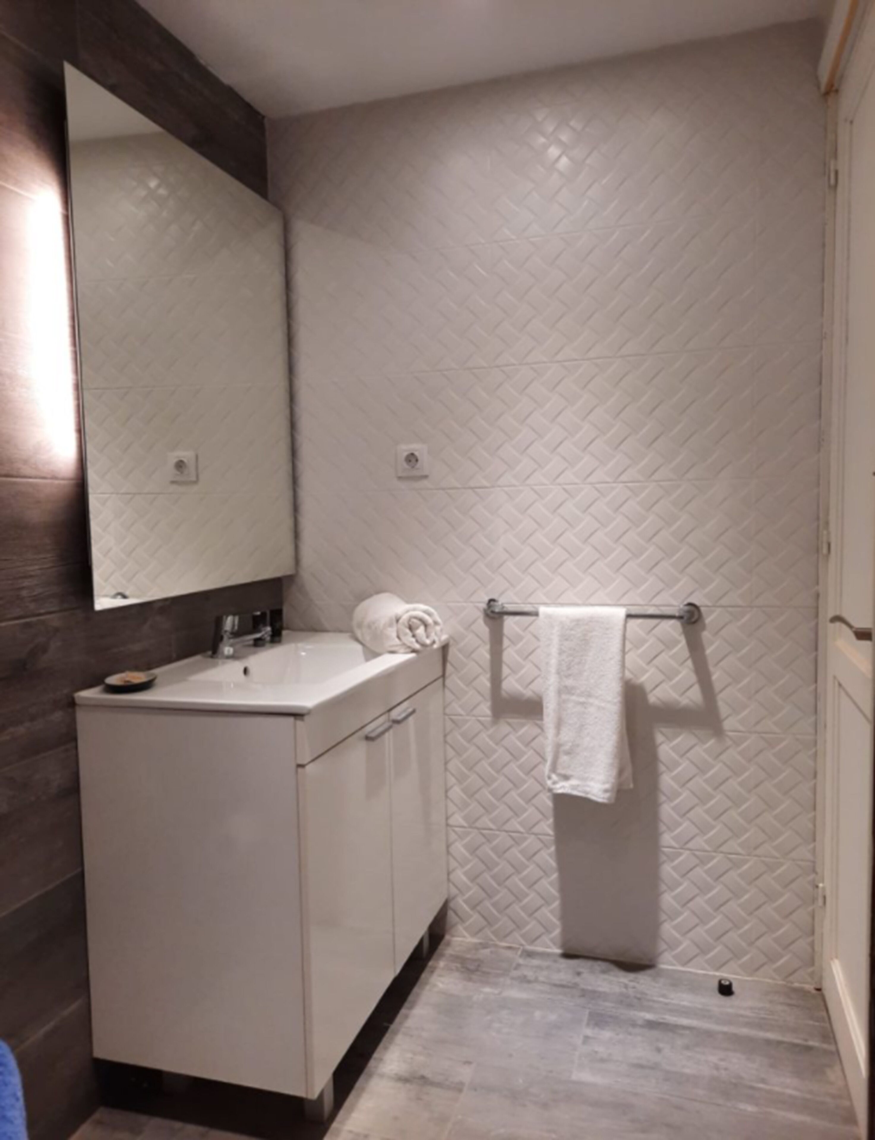 Un baño con un lavamanos blanco, espejo y toallero.