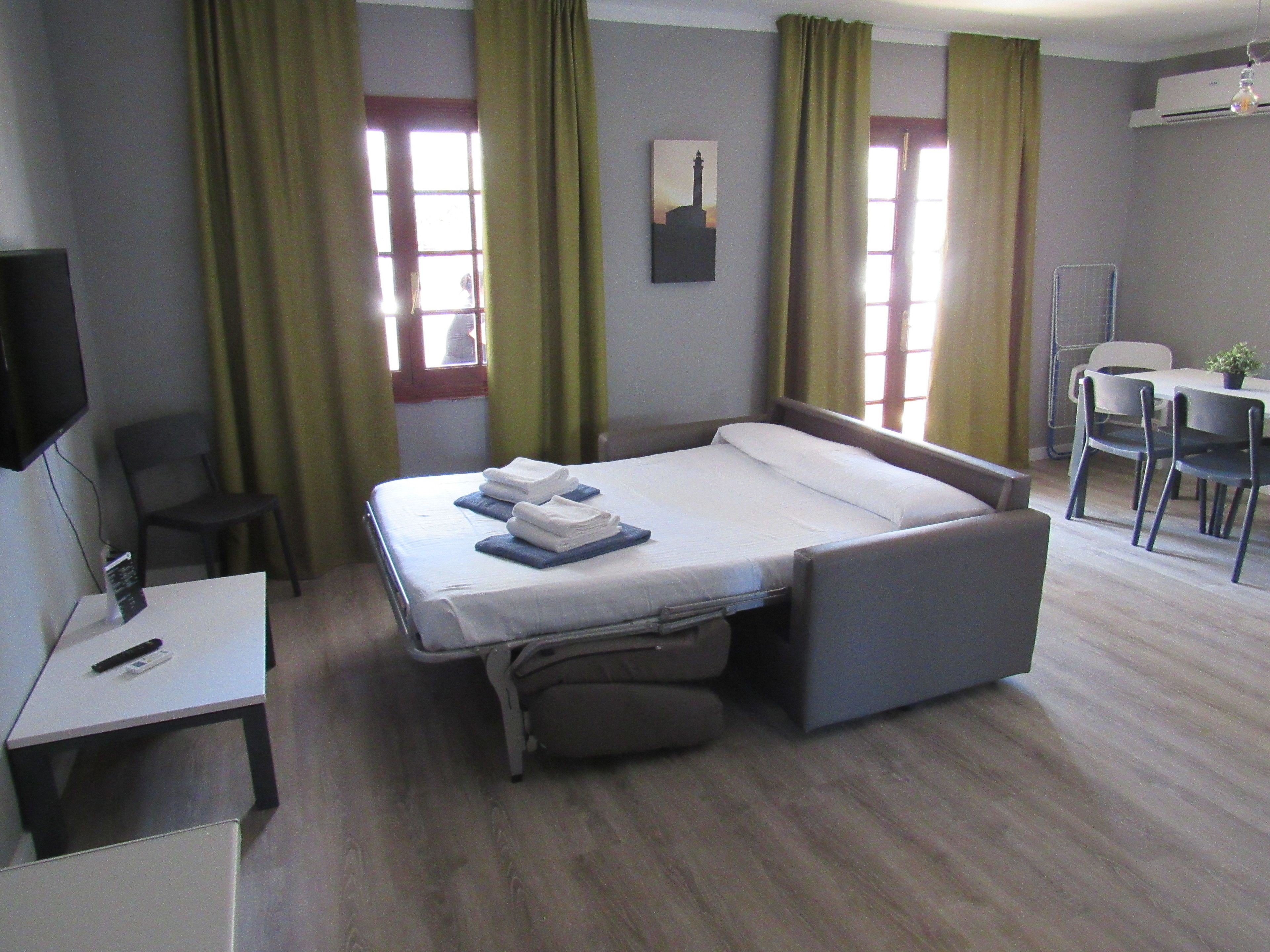 A hotel room with a bed, a desk, a chair, a table, and a TV.