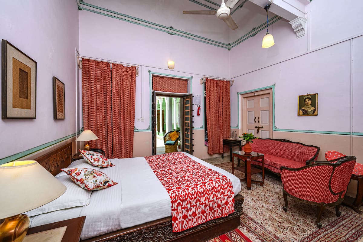 A hotel room with a bed, a desk, a chair, a sofa, and a ceiling fan.