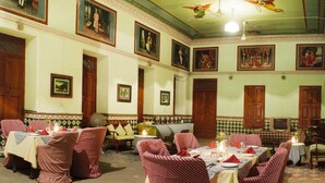 A dining area with multiple tables set for a meal, featuring traditional decor and artwork on the walls. - Neemrana's - Piramal Haveli (Jhunjhunu)