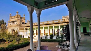 A covered outdoor seating area with a view of a historic building with domes and arches. - Neemrana's - Piramal Haveli (Jhunjhunu)