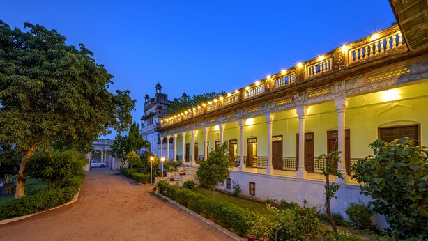 A historic building with a covered walkway, columns, and potted plants. - Neemrana's - Piramal Haveli (Jhunjhunu)