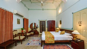 A bedroom with a bed, bedside table, lamp, and a mirror. - Neemrana's - Piramal Haveli (Jhunjhunu)