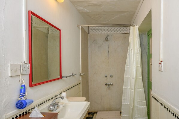A bathroom with a white sink, a mirror with a red frame, a shower with a white curtain, and a green door.