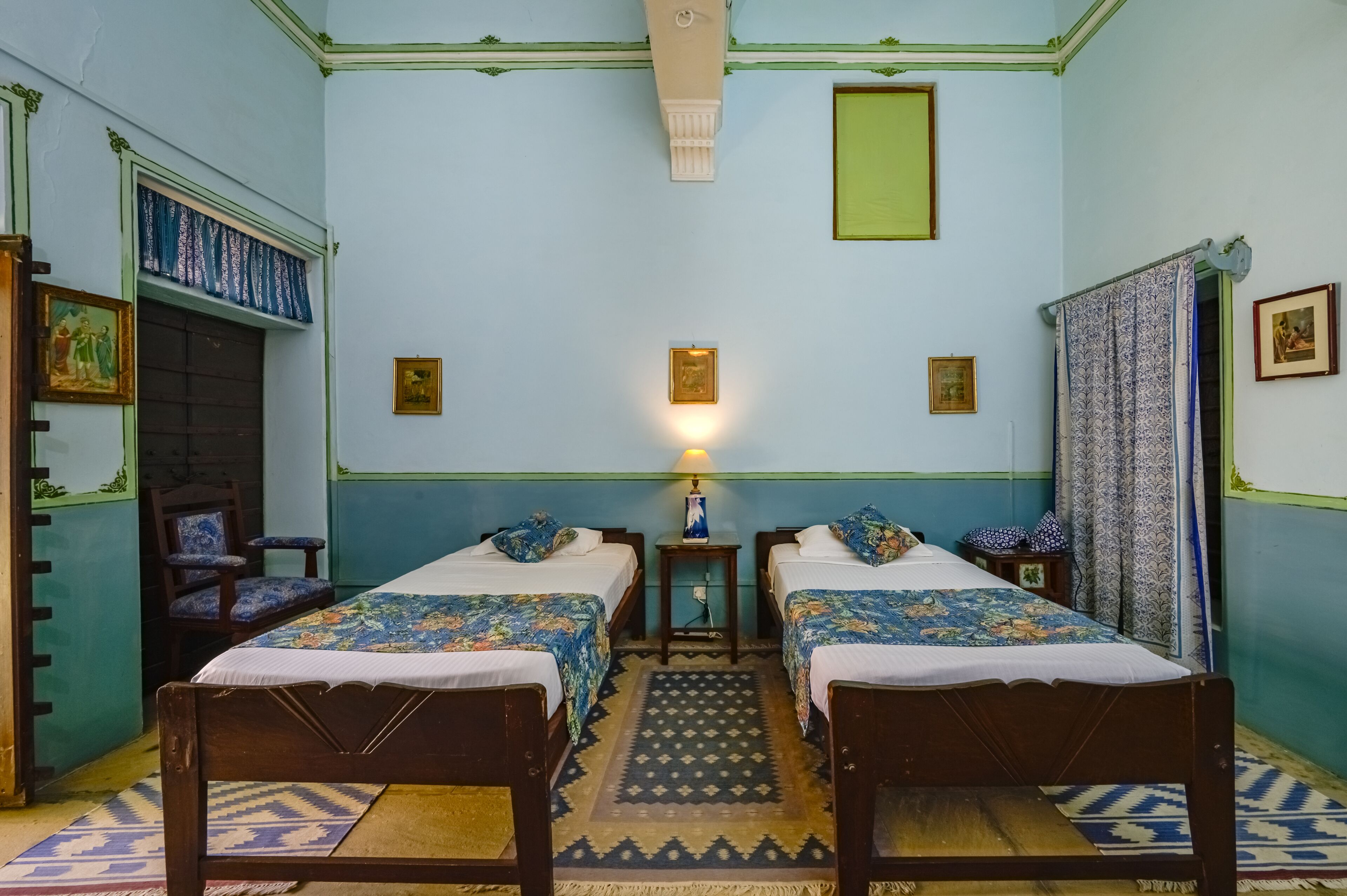 A room with two wooden beds, a small table with a lamp, and a chair.