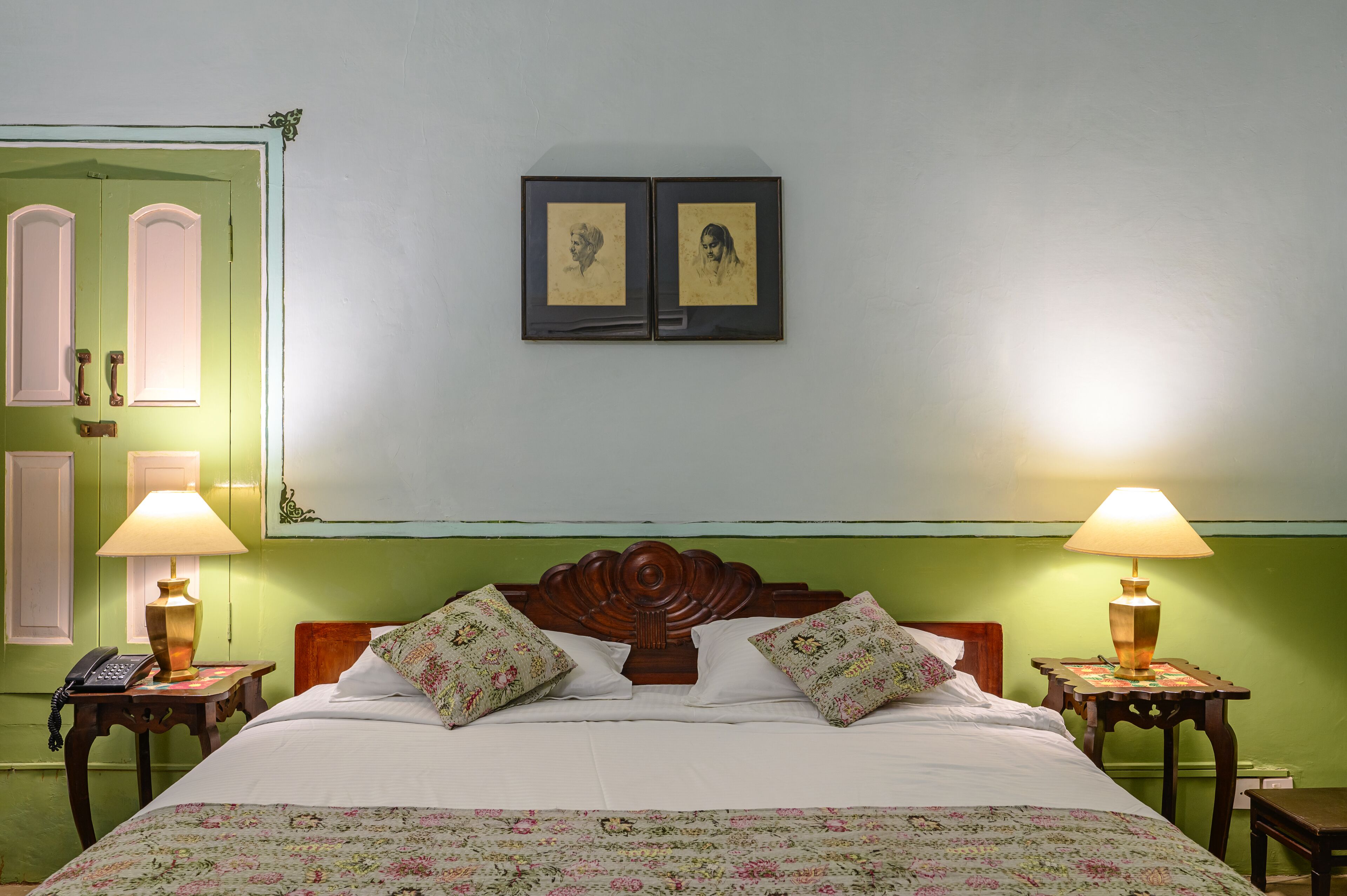 A room with a bed, two bedside tables with lamps, a green wall, and a door with a light switch.