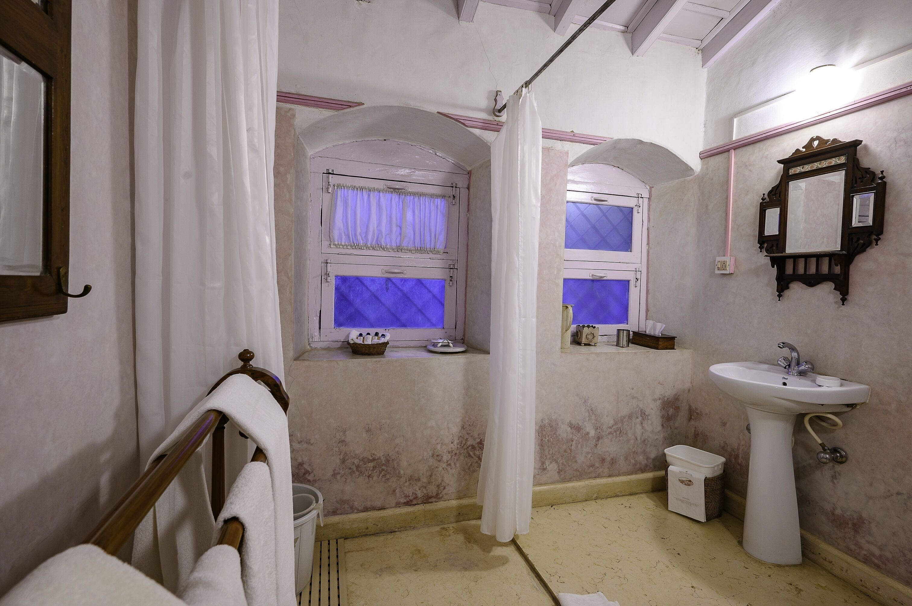 Baño con lavamanos, espejo y dos ventanas con cortinas.