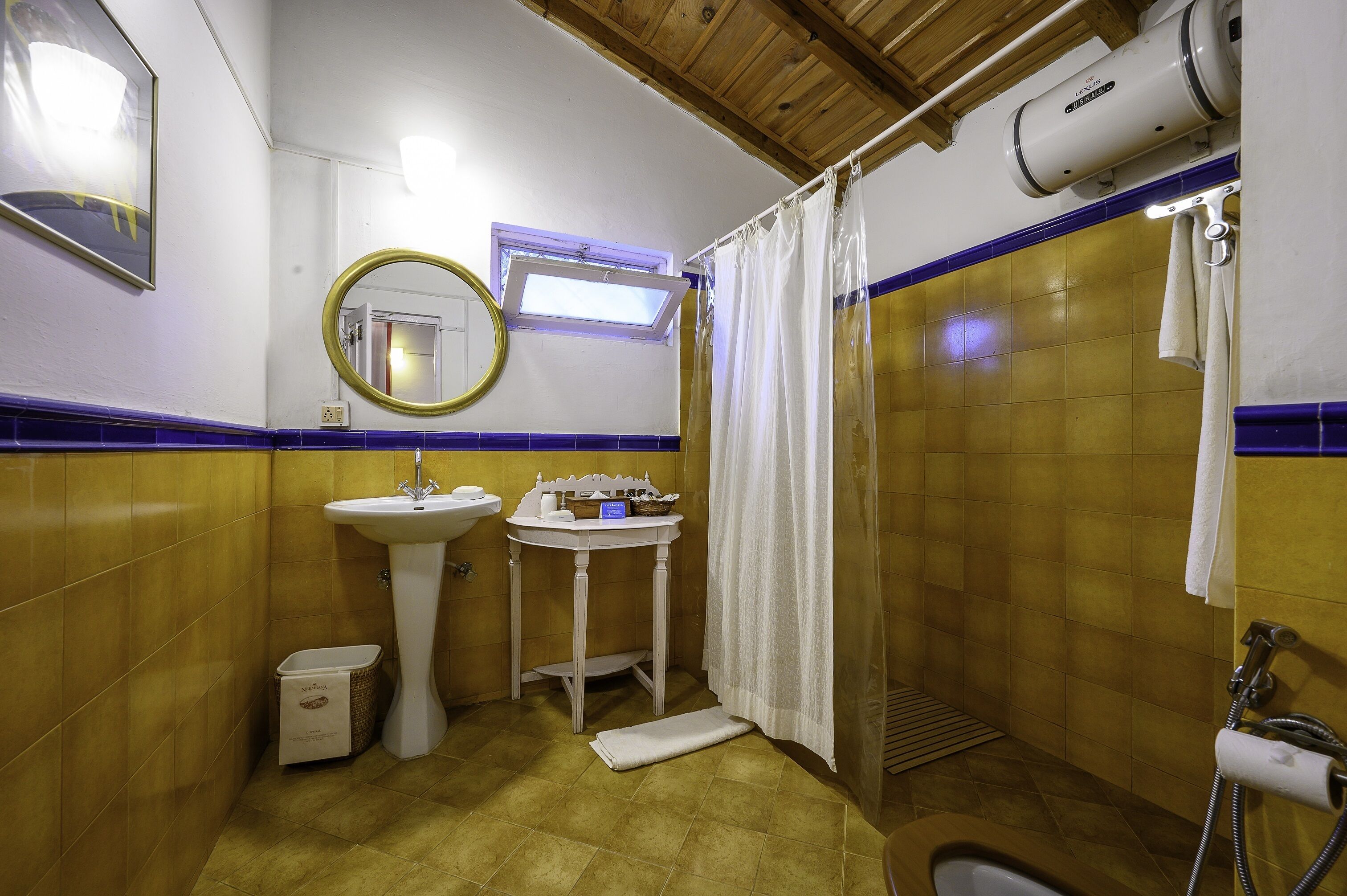 A bathroom with yellow tiled walls, a sink, a mirror, a shower, and a towel rack.