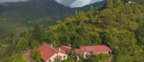 A rural setting with two houses on a hillside, surrounded by dense forest and mountains.