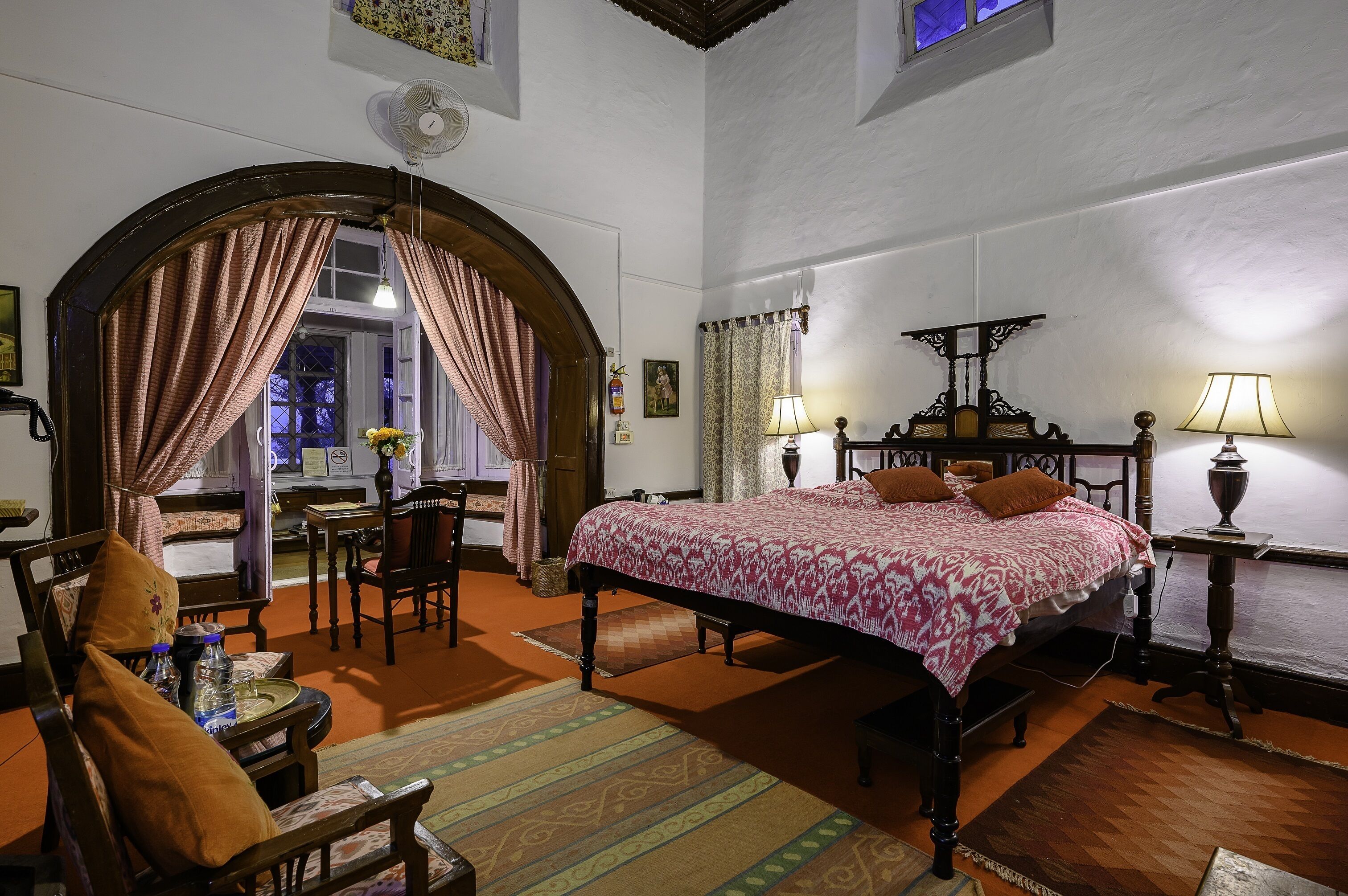 A bedroom with a large bed, a desk, a chair, and a window with curtains.