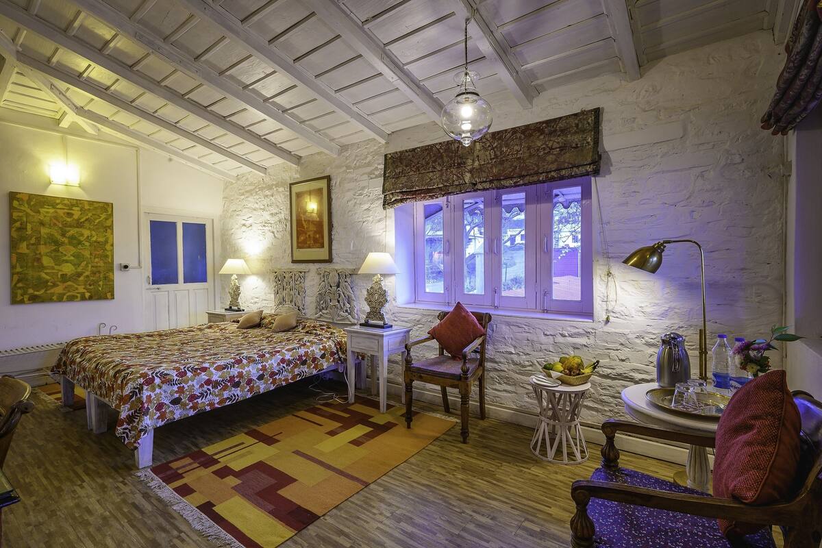 Un dormitorio acogedor con cama, una silla, una mesita y una ventana con cortinas.