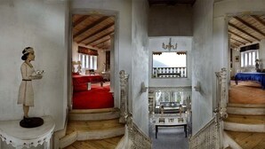 A corridor with a staircase leading to two rooms, each with a bed and a table. - Neemrana's - Ramgarh Bungalows (Kosiyakutoli)
