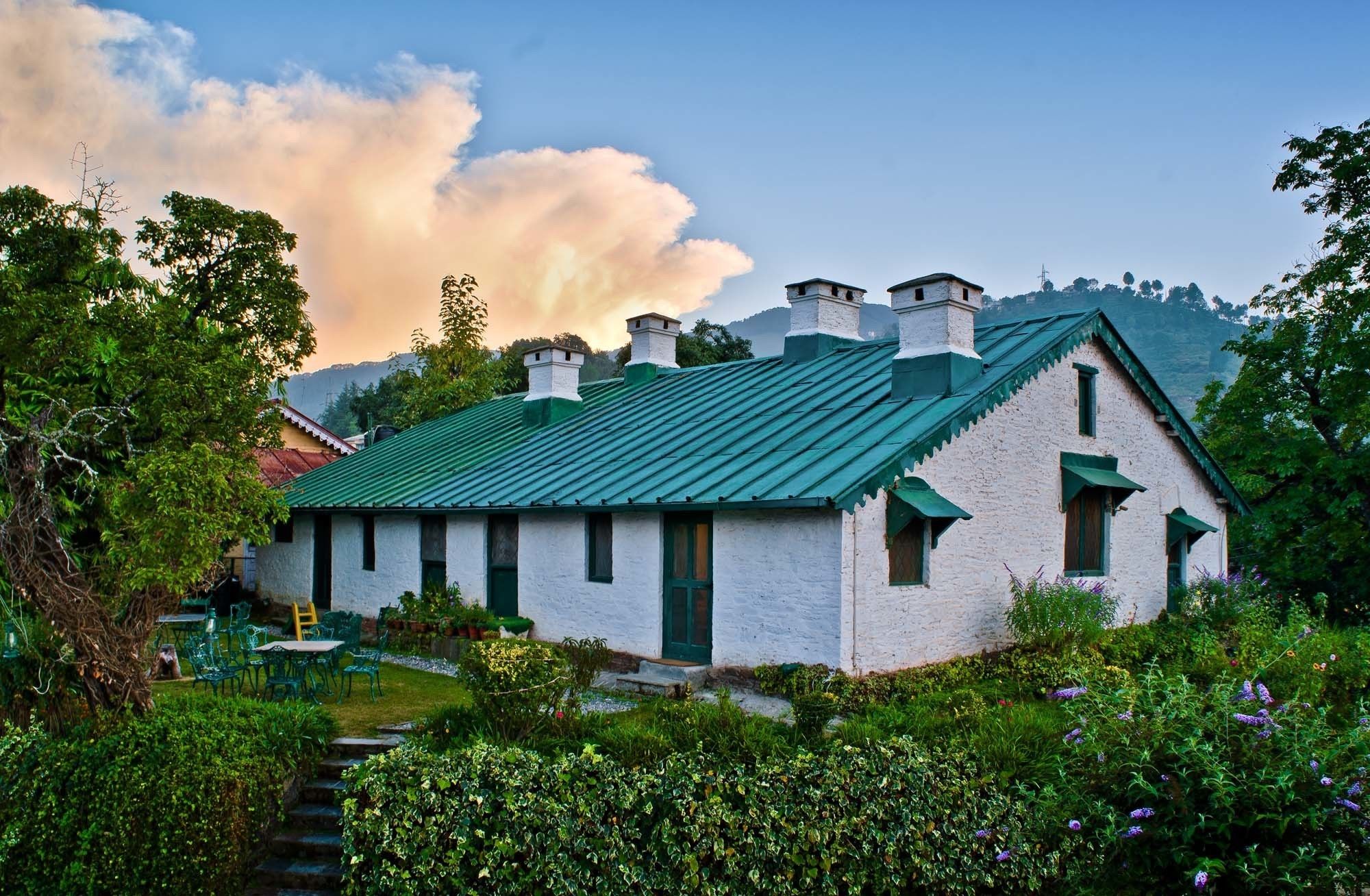 A white building with a green roof, surrounded by lush greenery and a clear sky.