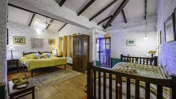 Una habitación rústica con vigas de madera a la vista, una cama con cubrecama amarillo, un armario de madera y una mesita con una cesta de fruta.