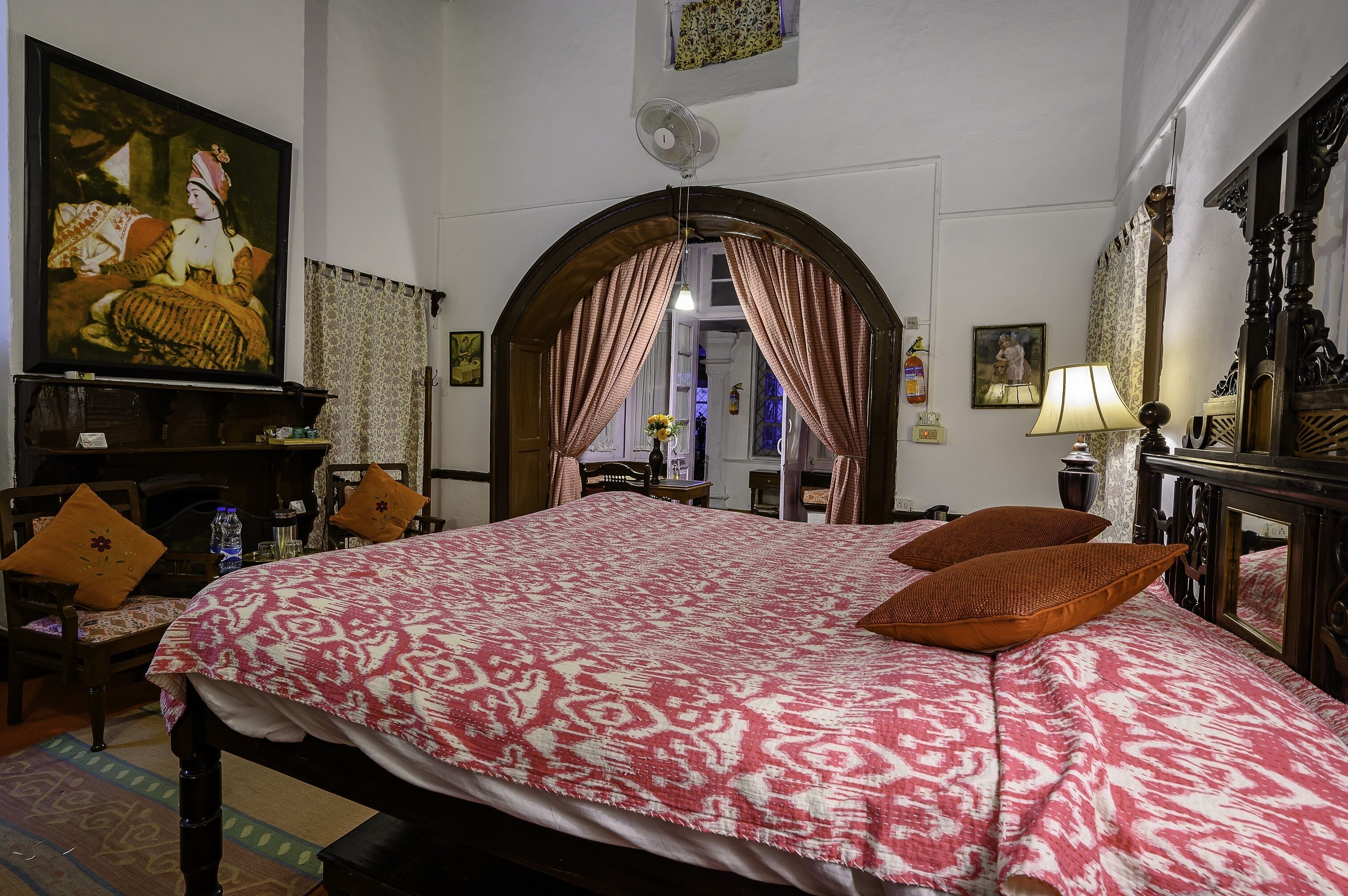 A hotel room with a large bed, a television, a fan, and a mirror.