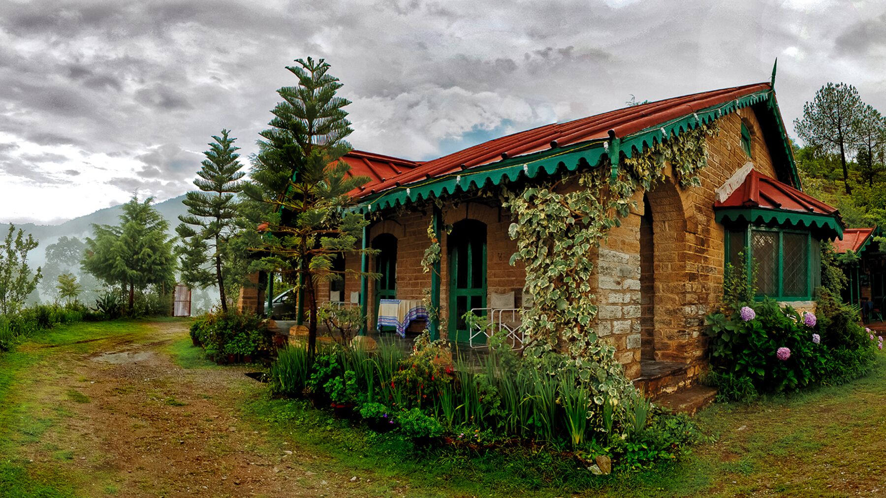 Una casa in pietra rustica con tetto rosso, immersa nel verde e circondata da alberi.
