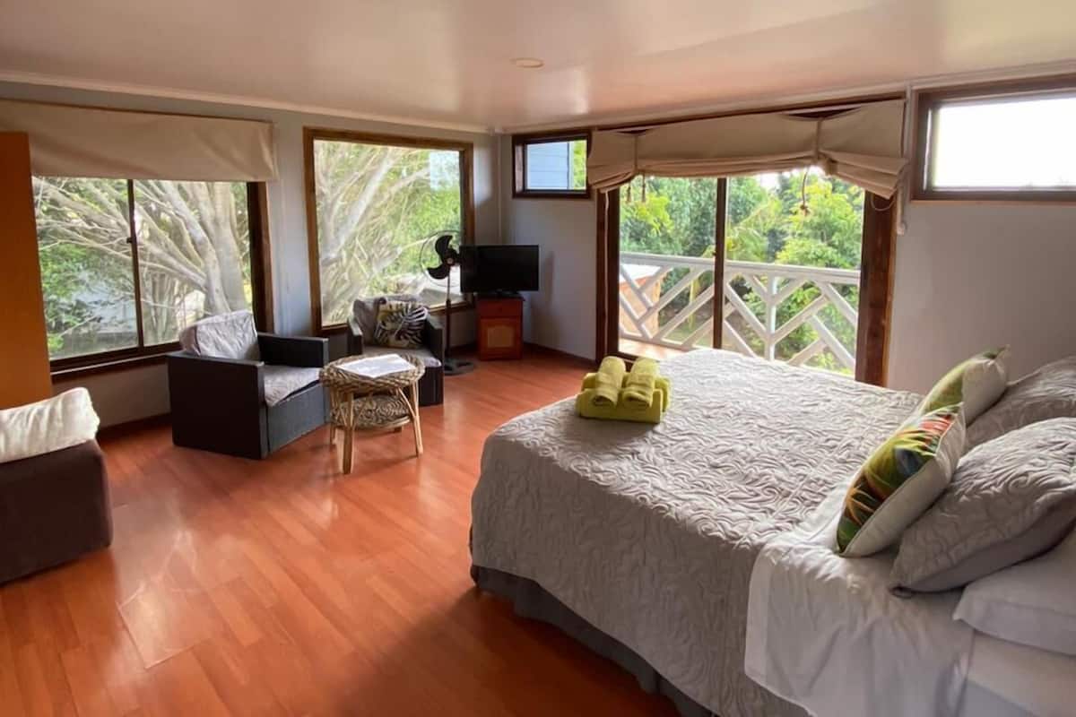 A spacious bedroom with a large bed, a seating area with a sofa and armchair, and a TV.