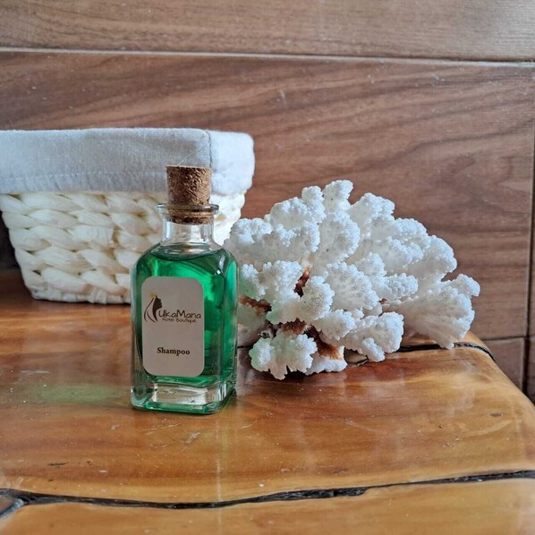 A bottle of shampoo on a wooden surface with a white textured object and a white coral-like structure in the background. - Hotel Uka Mana (Hanga Roa)