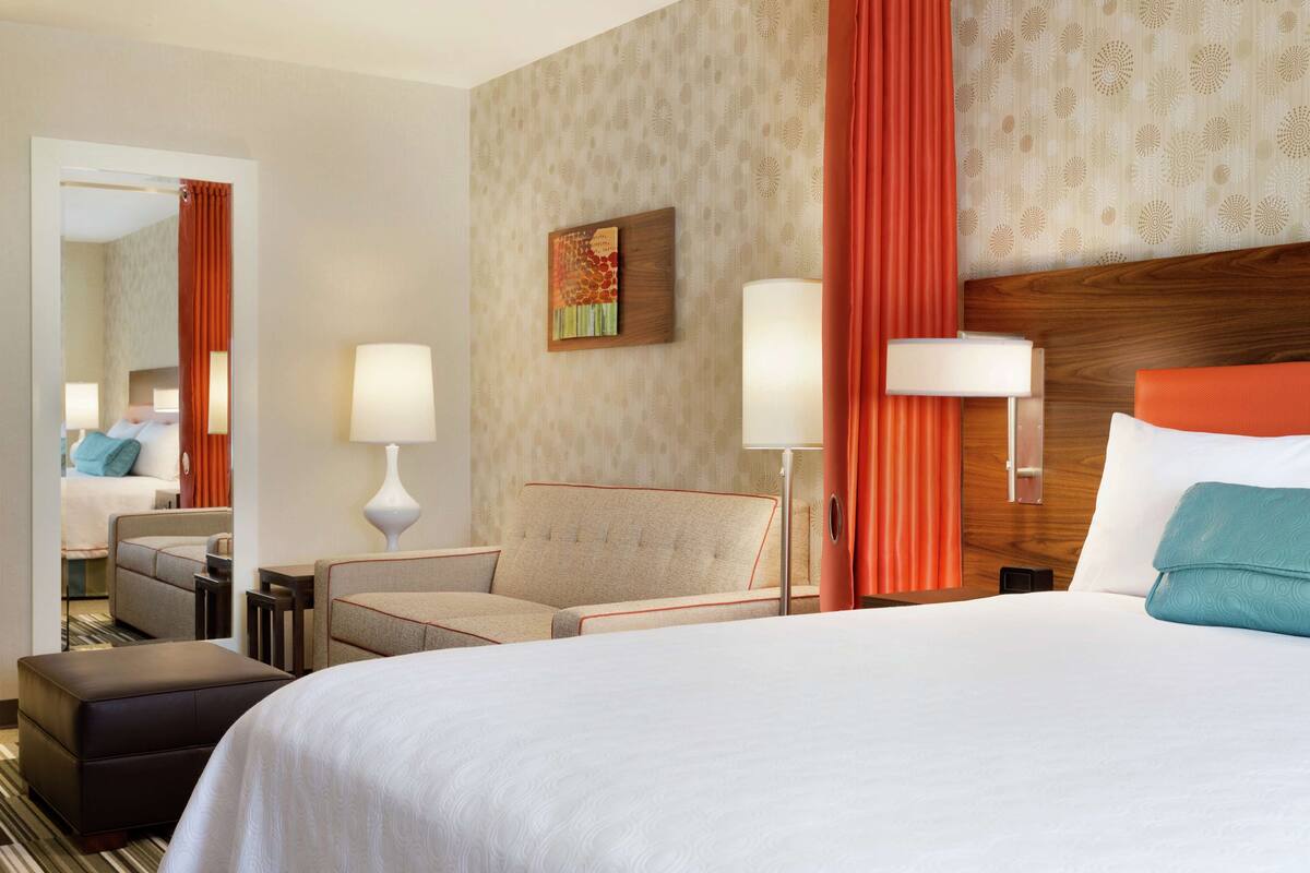 A hotel room with a large bed, a sofa, a chair, a small table, and a mirror.