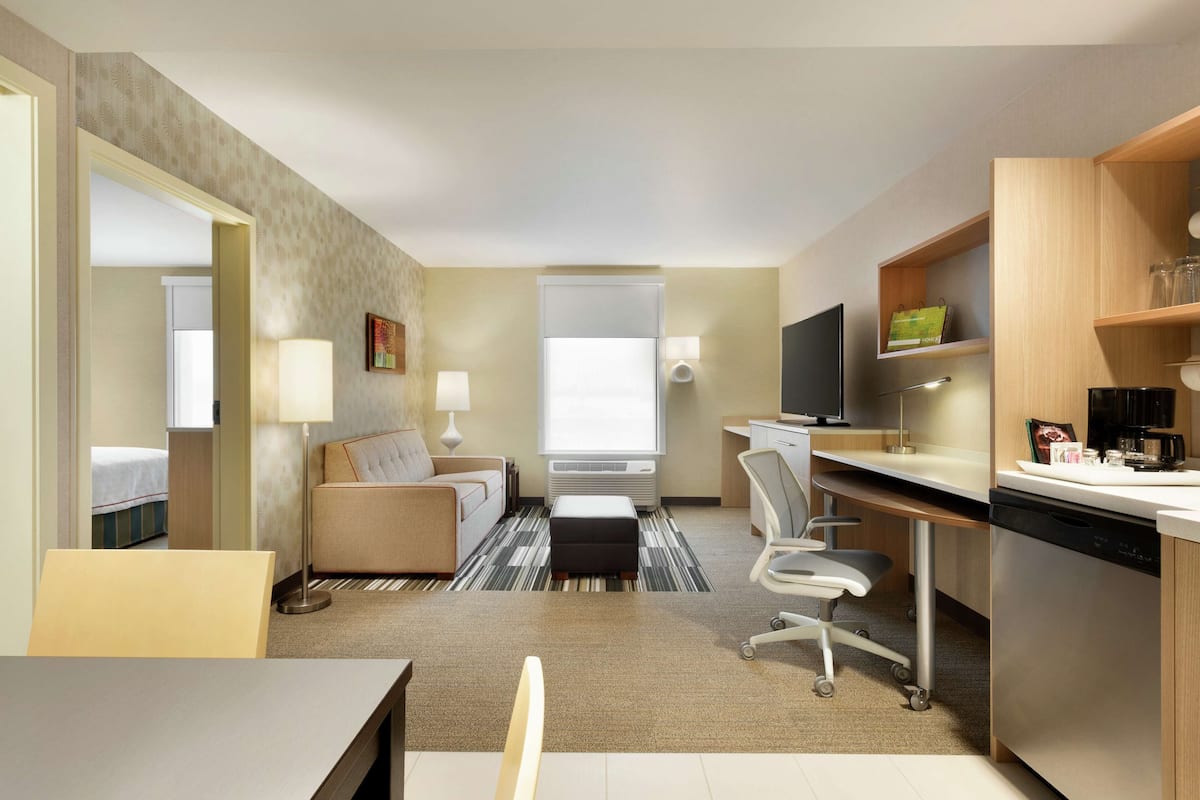 A hotel room with a bed, a sofa, a desk, a chair, a TV, a coffee maker, and a window.