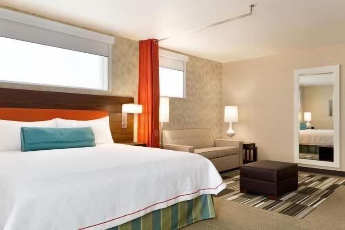 A hotel room with a bed, a chair, a desk, a mirror, and a window.