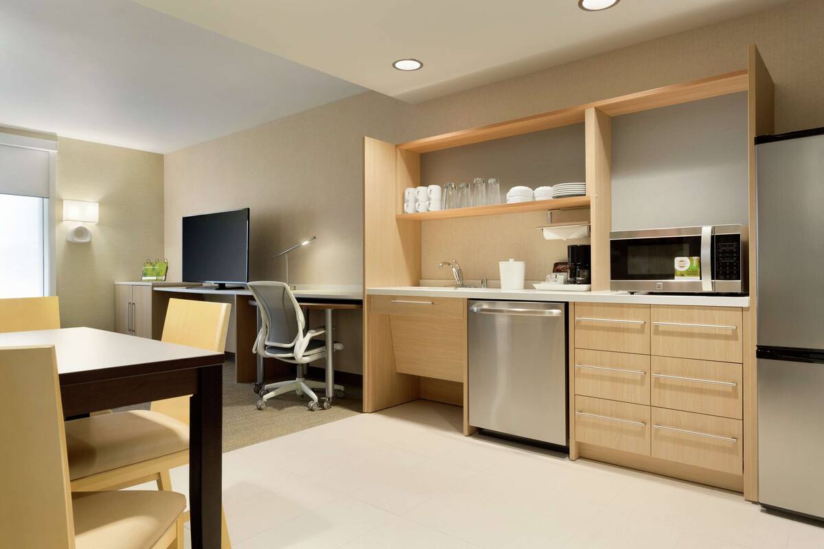 A modern kitchen with a dining area, including a desk, chair, and a television.