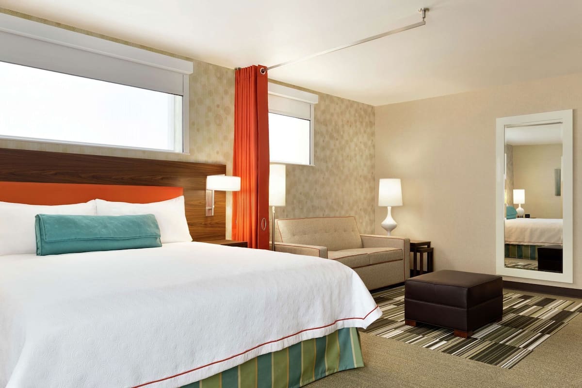 Une chambre d’hôtel avec un lit, un canapé, une petite table, un miroir et une fenêtre avec des rideaux.