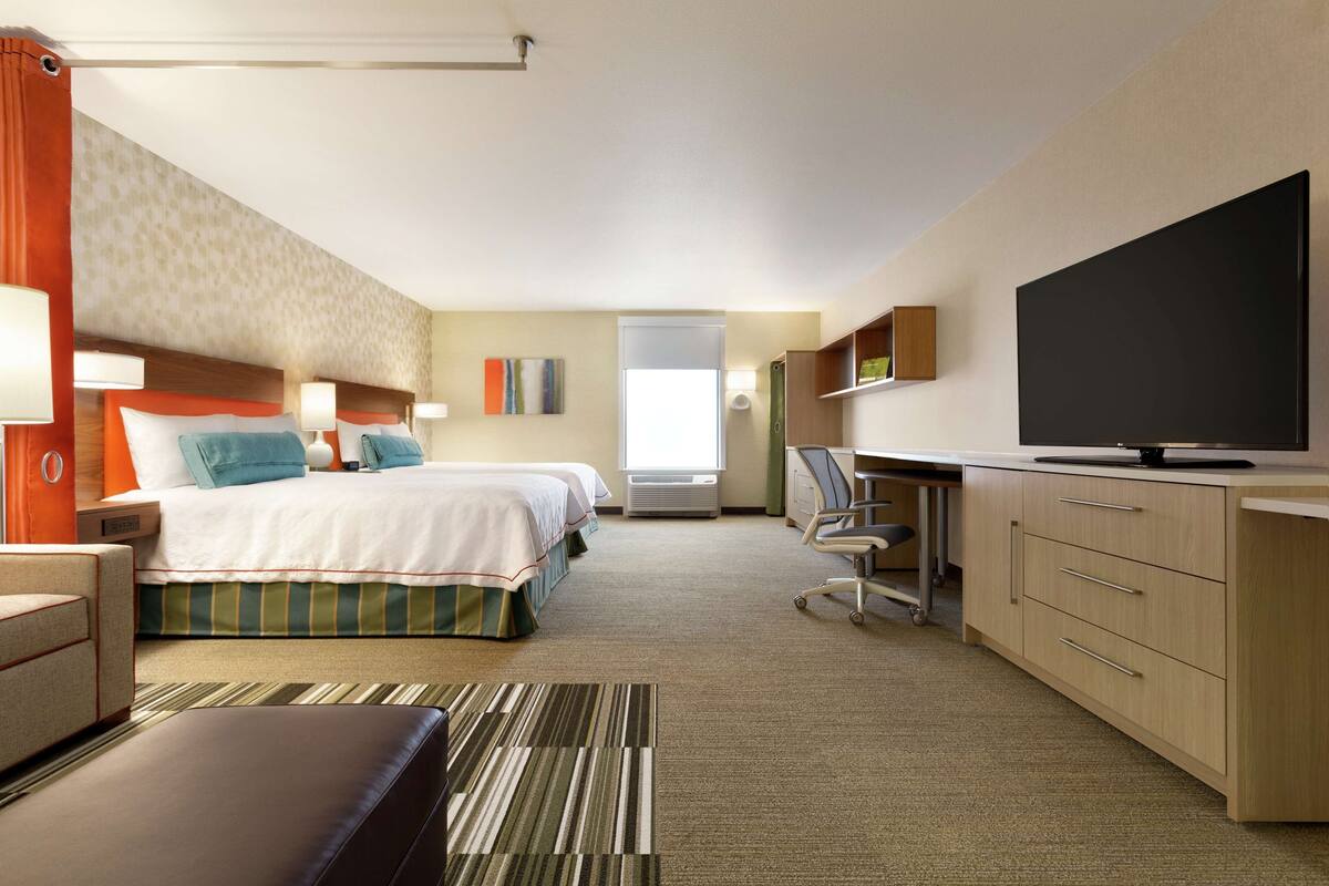 A hotel room with two beds, a desk, a TV, and a bathroom visible through an open door.