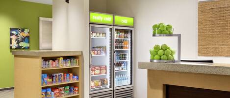 A hotel reception area with a counter, two refrigerators labeled "really cold" and "cold," and a shelf with green apples.