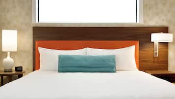 A hotel room with a large bed, a wooden headboard, a teal throw pillow, and a nightstand with a lamp.