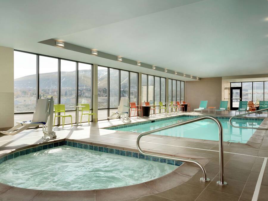 Una piscina interna con diverse corsie, una vasca idromassaggio e aree relax con sedie.